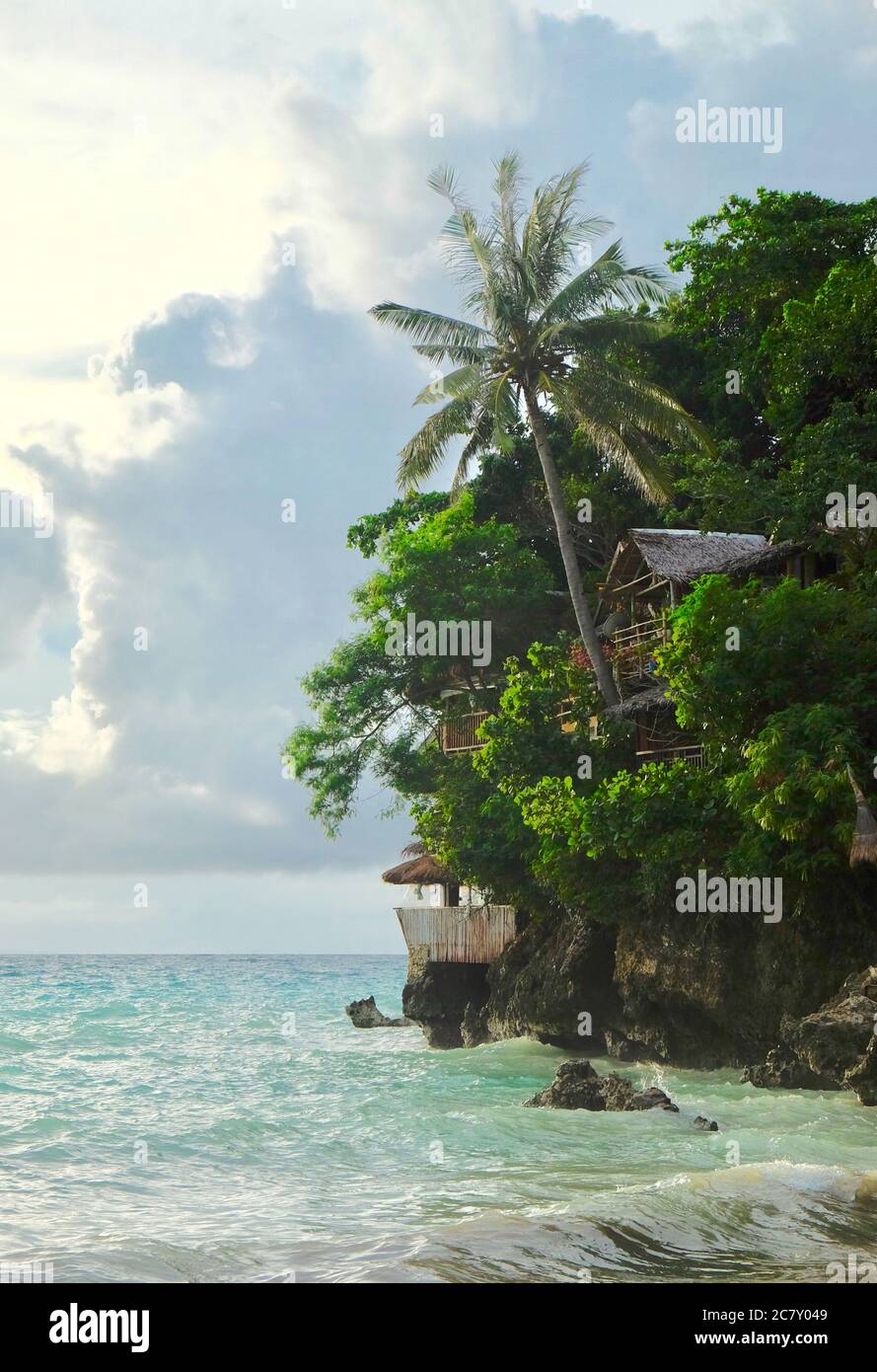 Cocotier vert et cabane en rondins sur la falaise au-dessus de l'océan vert. Magnifique ciel blanc nuageux et ensoleillé. Un coin de l'île Boracay aux Philippines. Banque D'Images