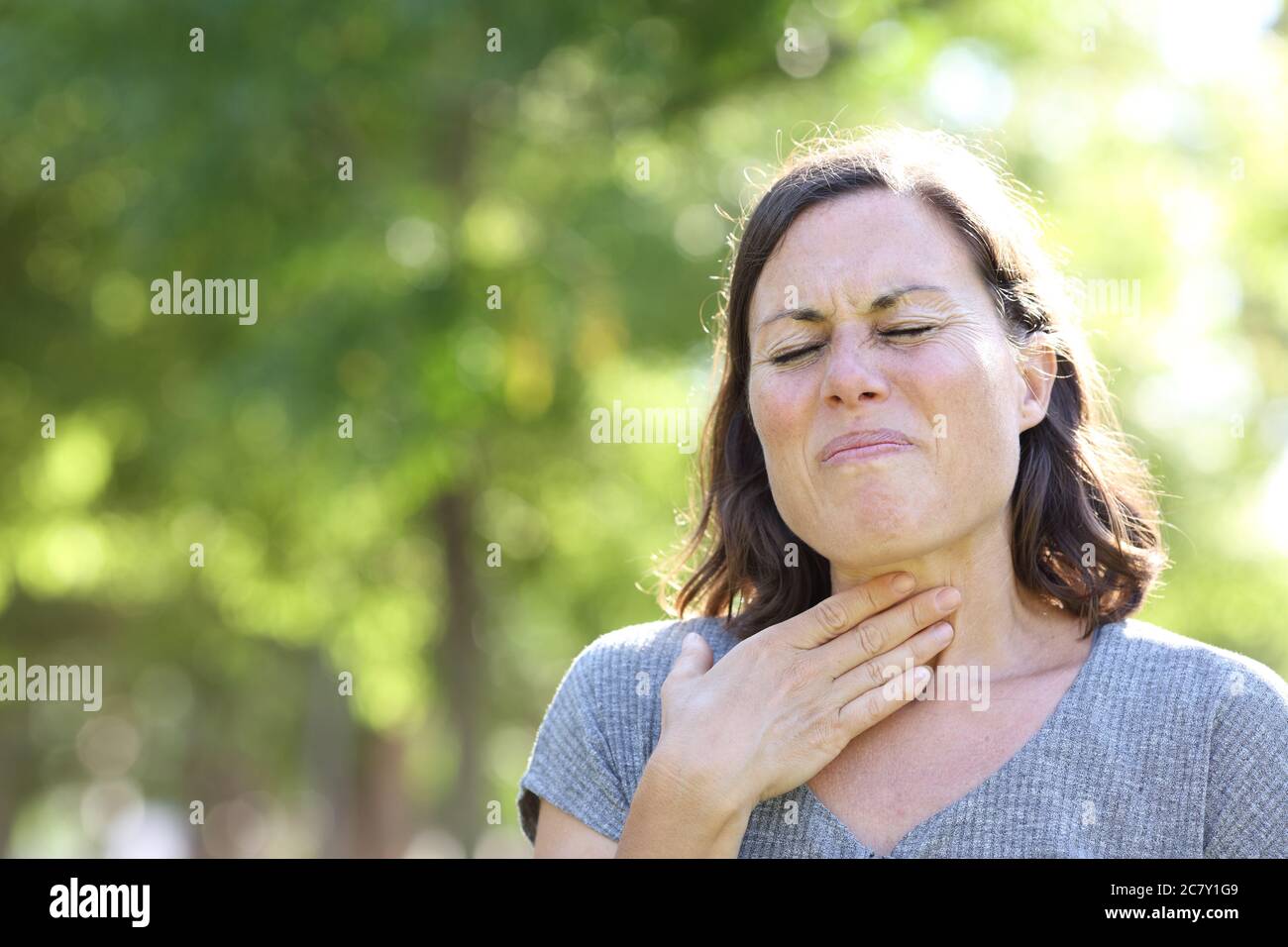 Femme d'âge moyen en douleur souffrant d'un mal de gorge dans le parc en été Banque D'Images