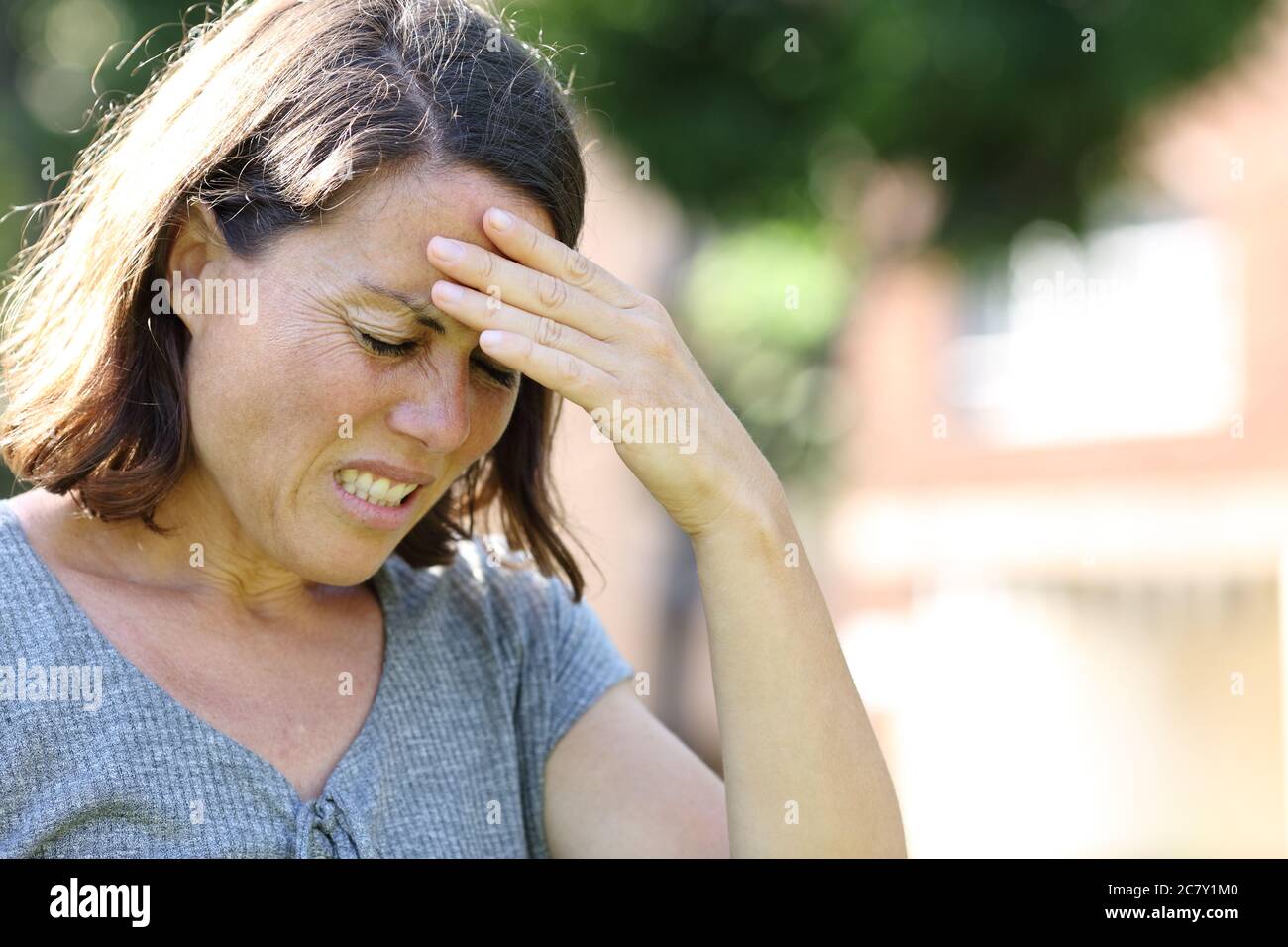 Femme adulte en douleur souffrant de maux de tête debout dans un parc en été Banque D'Images