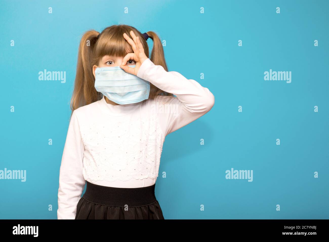 Petite fille portant un masque médical montrer le symbole OK doigt mains geste pour arrêter l'épidémie de virus corona isolé sur bleu. Coronavirus et virus épidémiques s. Banque D'Images