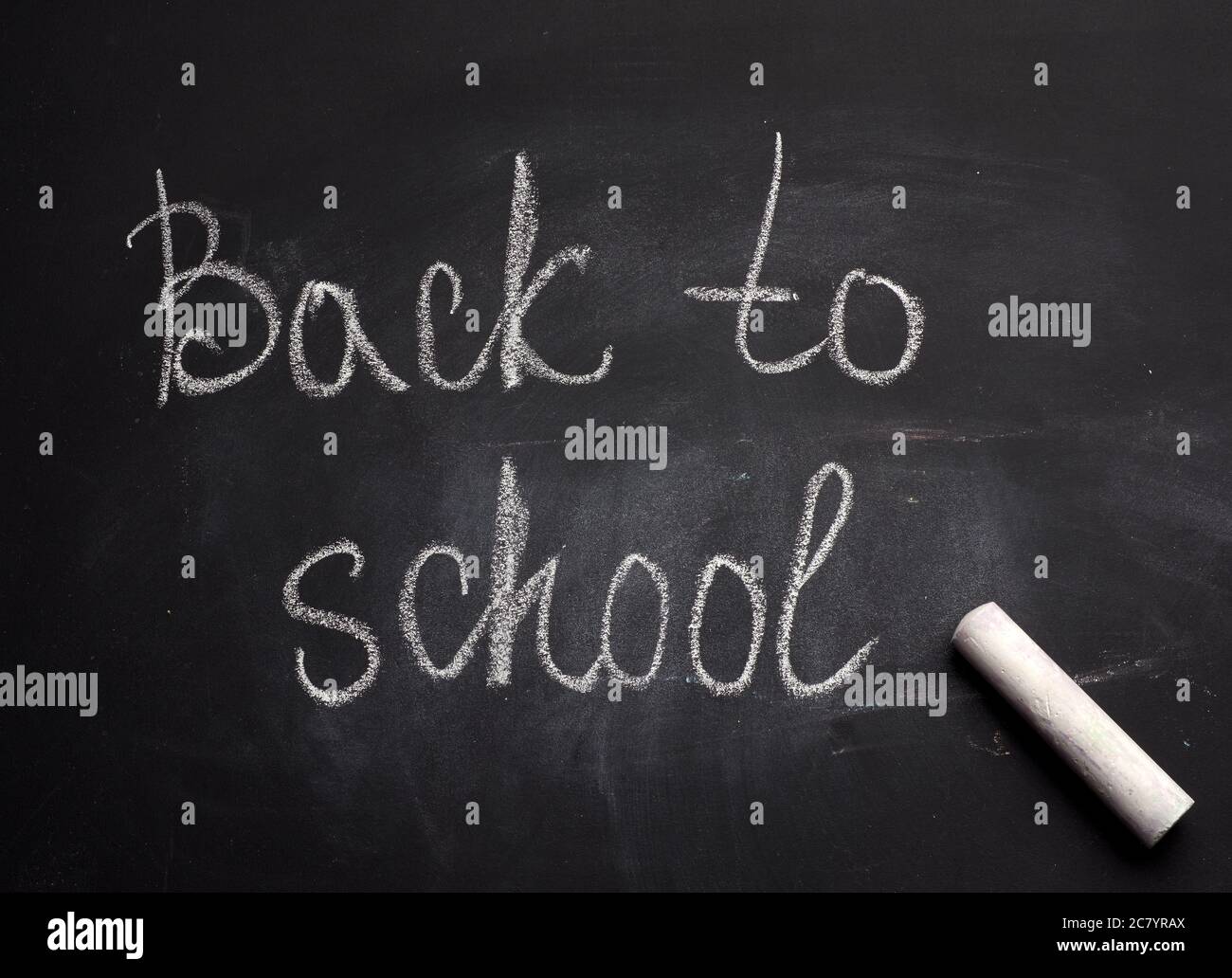 inscription de retour à l'école en craie blanche sur un conseil scolaire noir et un morceau de craie, gros plan Banque D'Images