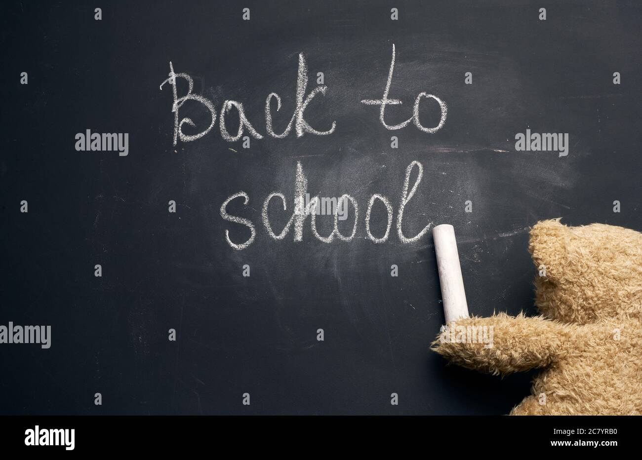 inscription à l'école en craie blanche sur un conseil scolaire noir et un morceau de craie dans le paw d'un ours en peluche brun Banque D'Images