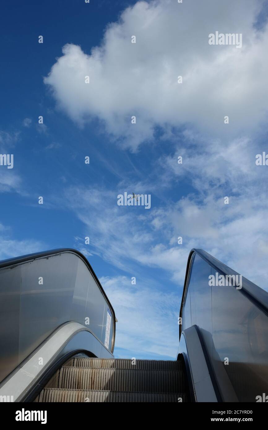Escalier roulant en plein air se lève vers le ciel bleu ensoleillé avec des nuages blancs. Un avion volant dans le ciel. Liberté, succès, concept de promotion Banque D'Images