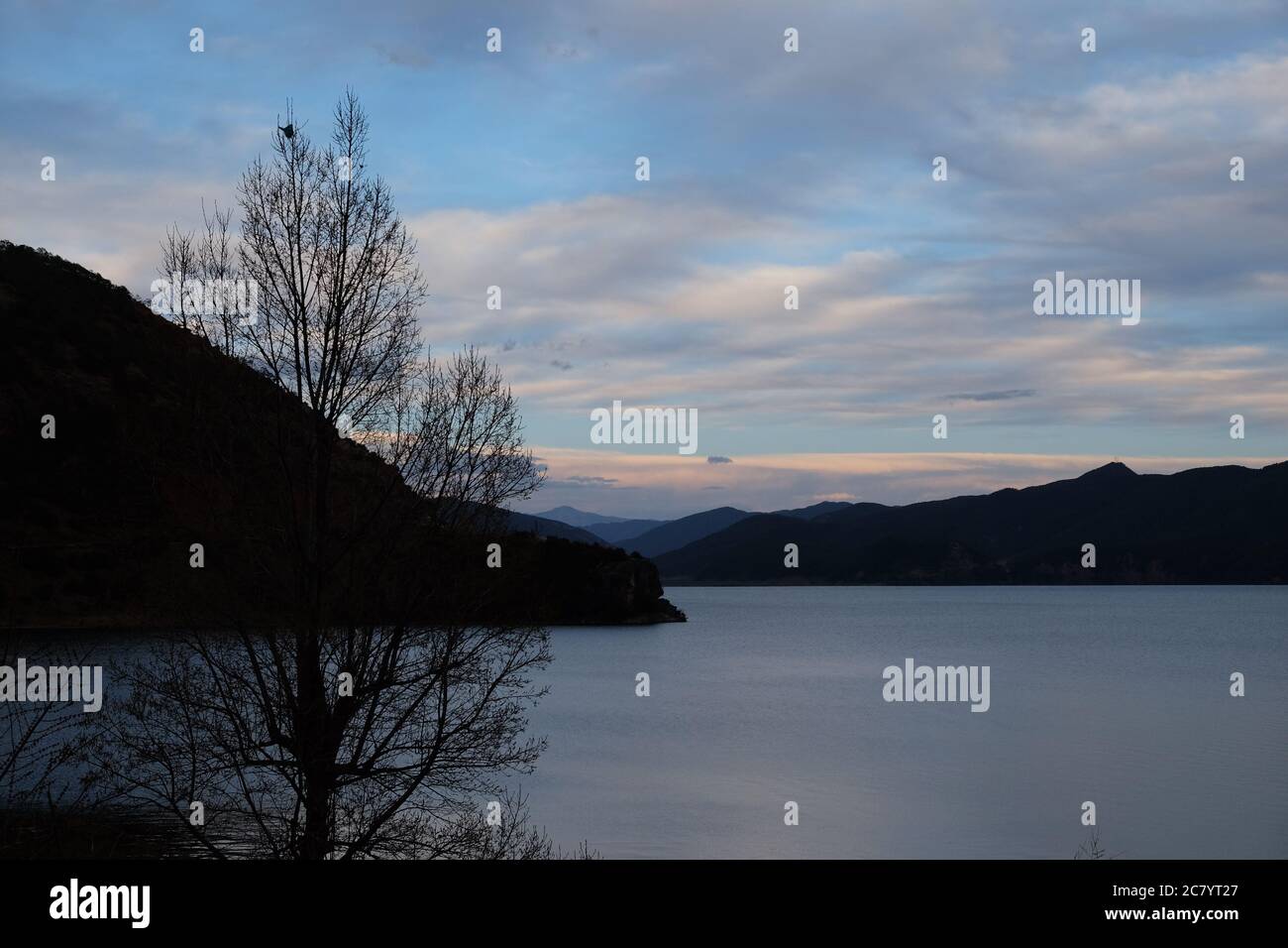 silhouette de montagnes et de branches d'arbres sur un large lac paisible. nuages blancs dans le ciel bleu au coucher du soleil. Dans le lac Lugu Yunnan Chine Banque D'Images