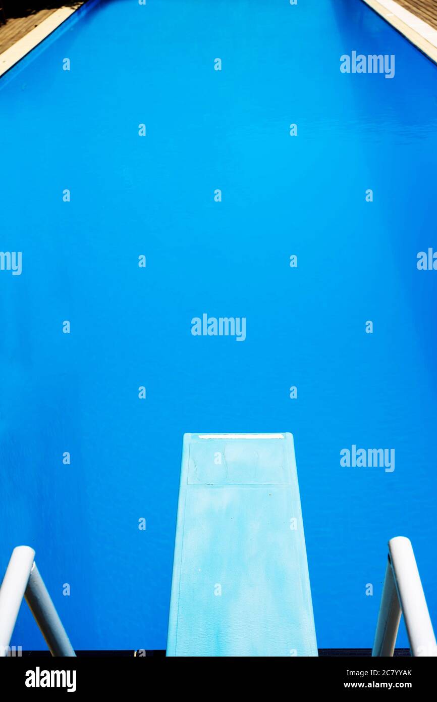 Vue d'en haut sur un plongeoir bleu clair et une piscine bleue avec une surface d'eau calme au soleil. Banque D'Images