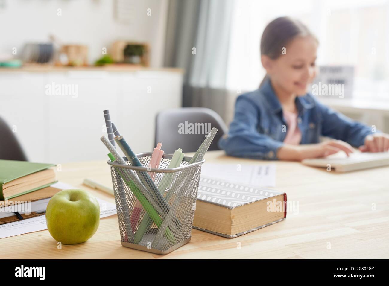 Image d'arrière-plan de la fille utilisant l'ordinateur portable pendant l'étude à la maison, se concentrer sur le porte-crayon et les livres, l'espace de copie Banque D'Images