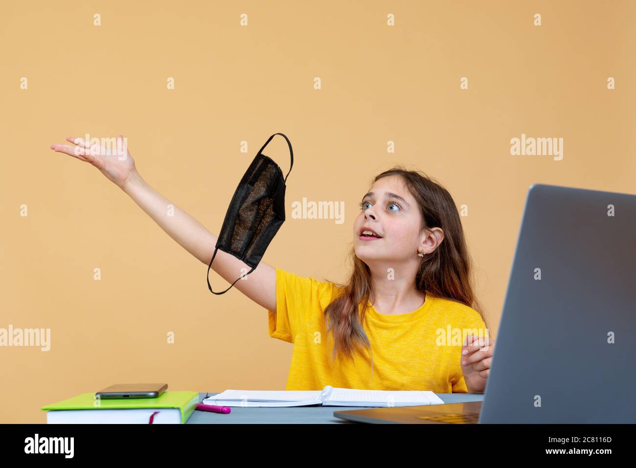 Une petite fille prend son masque médical stérile et ennuyeux sur fond orange. Bonne fin Banque D'Images