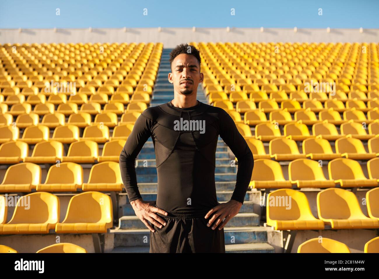 Un jeune sportif afro-américain regarde avec confiance les caméras parmi les sièges vides du stade Banque D'Images