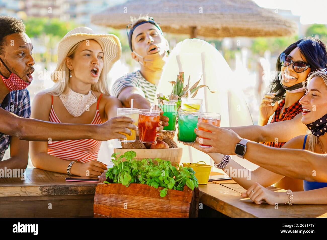 Amis multiethniques buvant des queues de cochon dans un bar de plage dehors en été avec masque de visage pour être protégé contre le coronavirus - heureux gens gaiin Banque D'Images