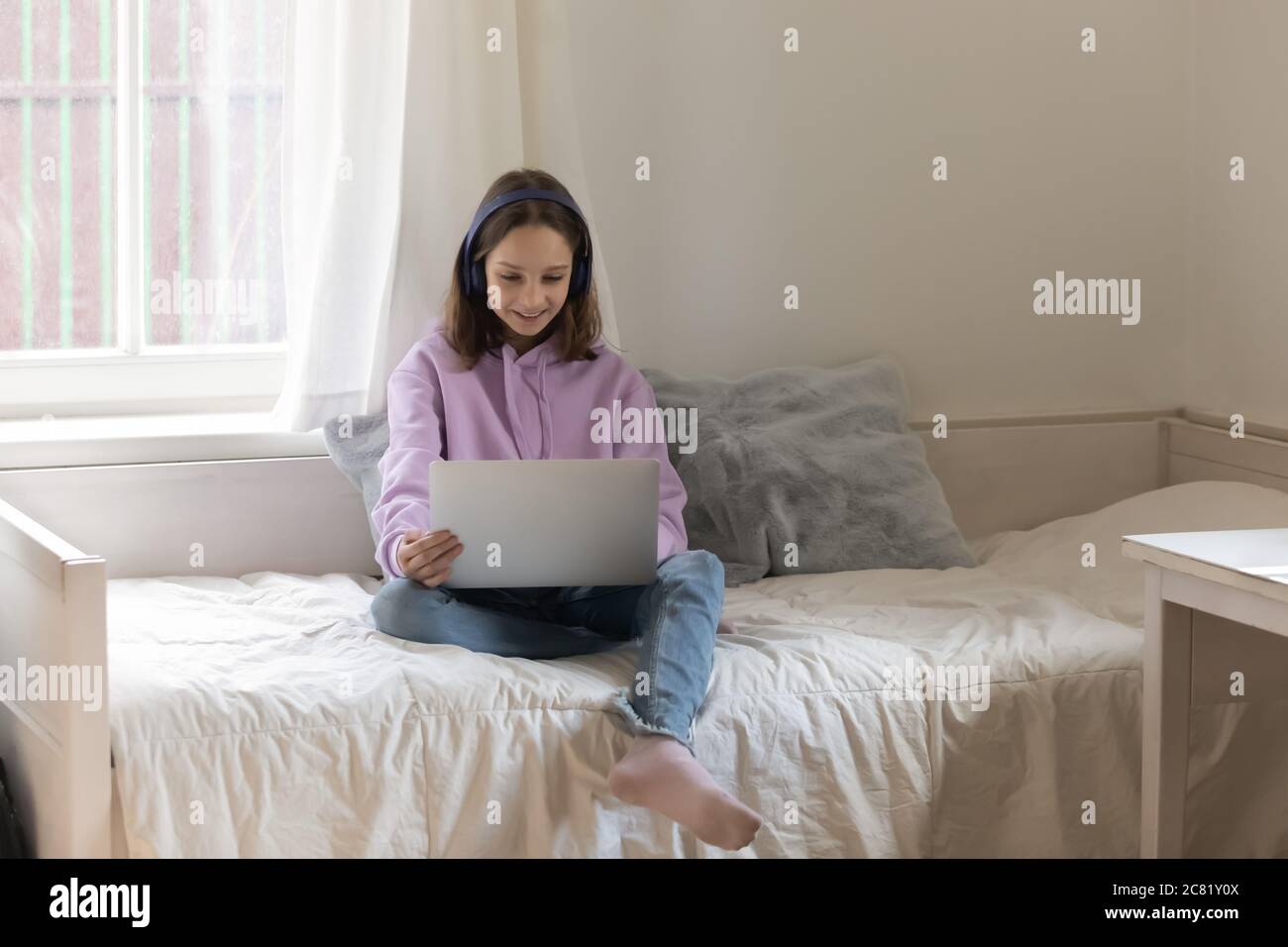 Une adolescente souriante portant un casque se détendant sur son lit avec un ordinateur portable Banque D'Images