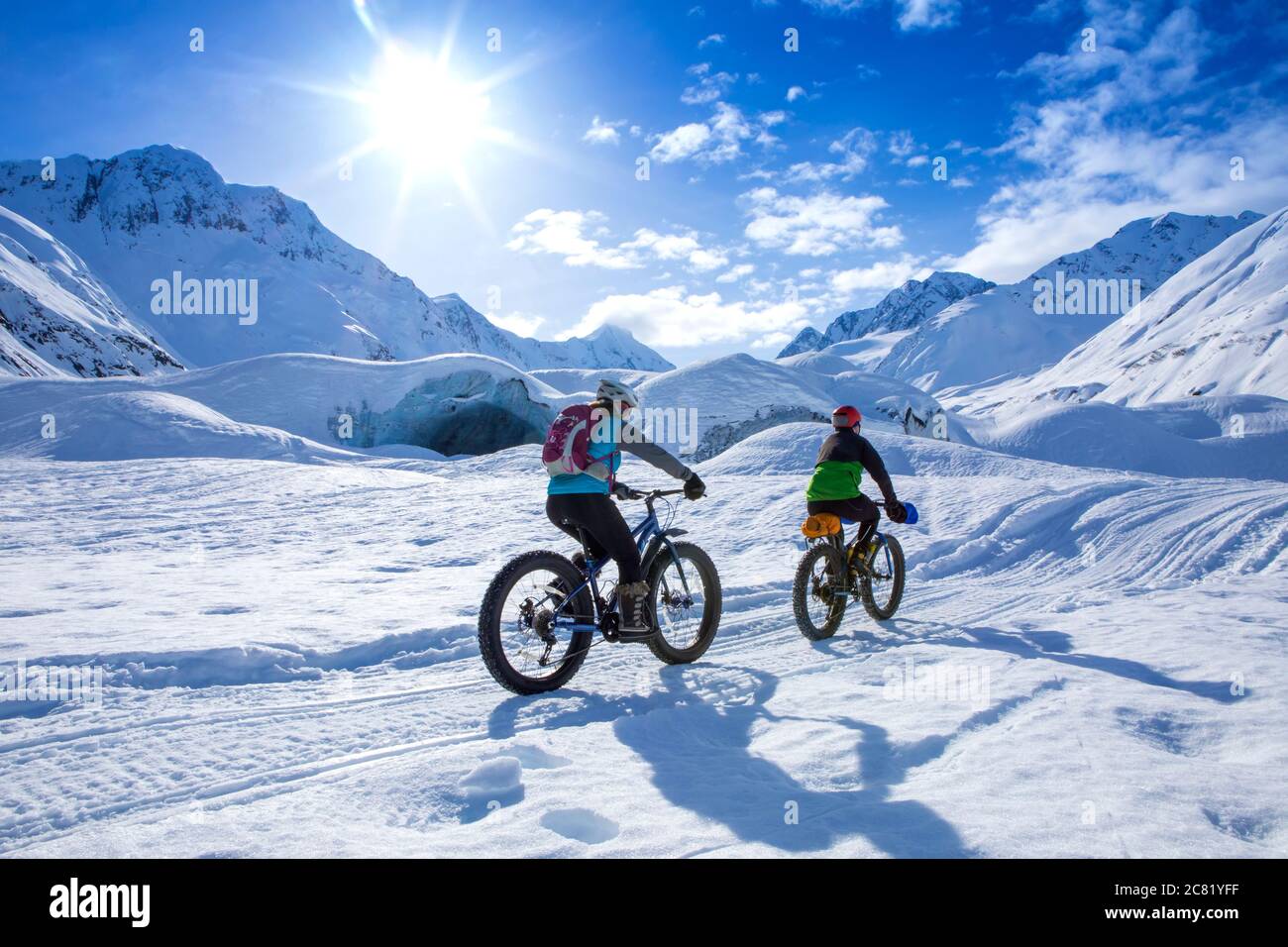 Deux femmes font du vélo gras en face du glacier Skookum, dans la forêt nationale de Chugach, en Alaska, par une journée d'hiver ensoleillée, qui se promènait en train de se déplacer Banque D'Images