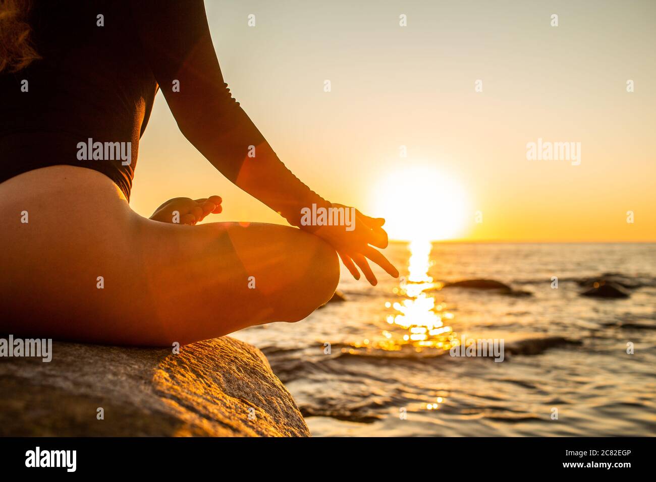 Main d'une femme méditant dans une pose de Lotus de yoga sur la plage au coucher du soleil. Fille assise sur un rocher chaud Banque D'Images