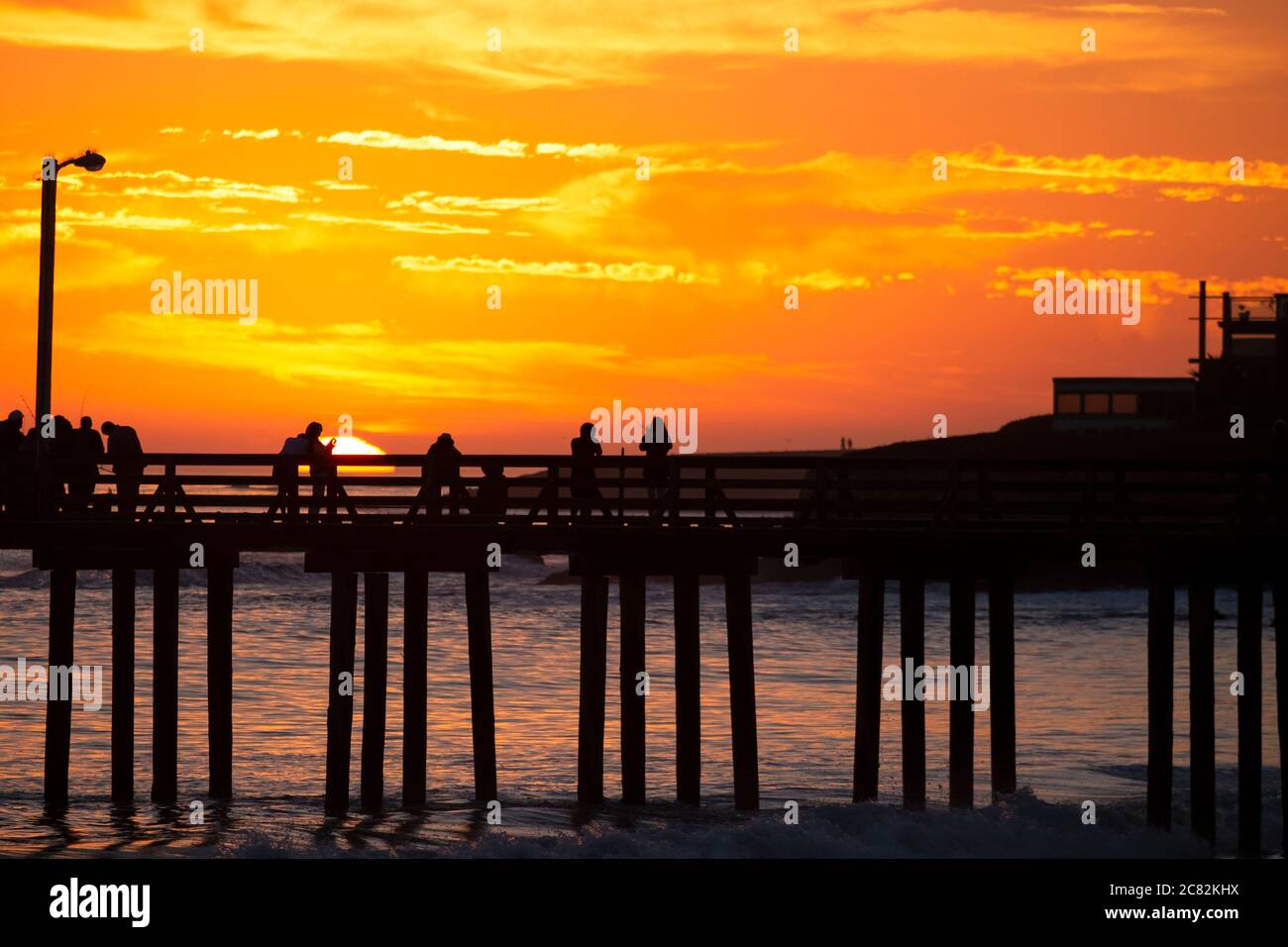 Groupe de personnes sur un quai regardant un coucher de soleil classique de la Californie dorée à Cayucos Banque D'Images