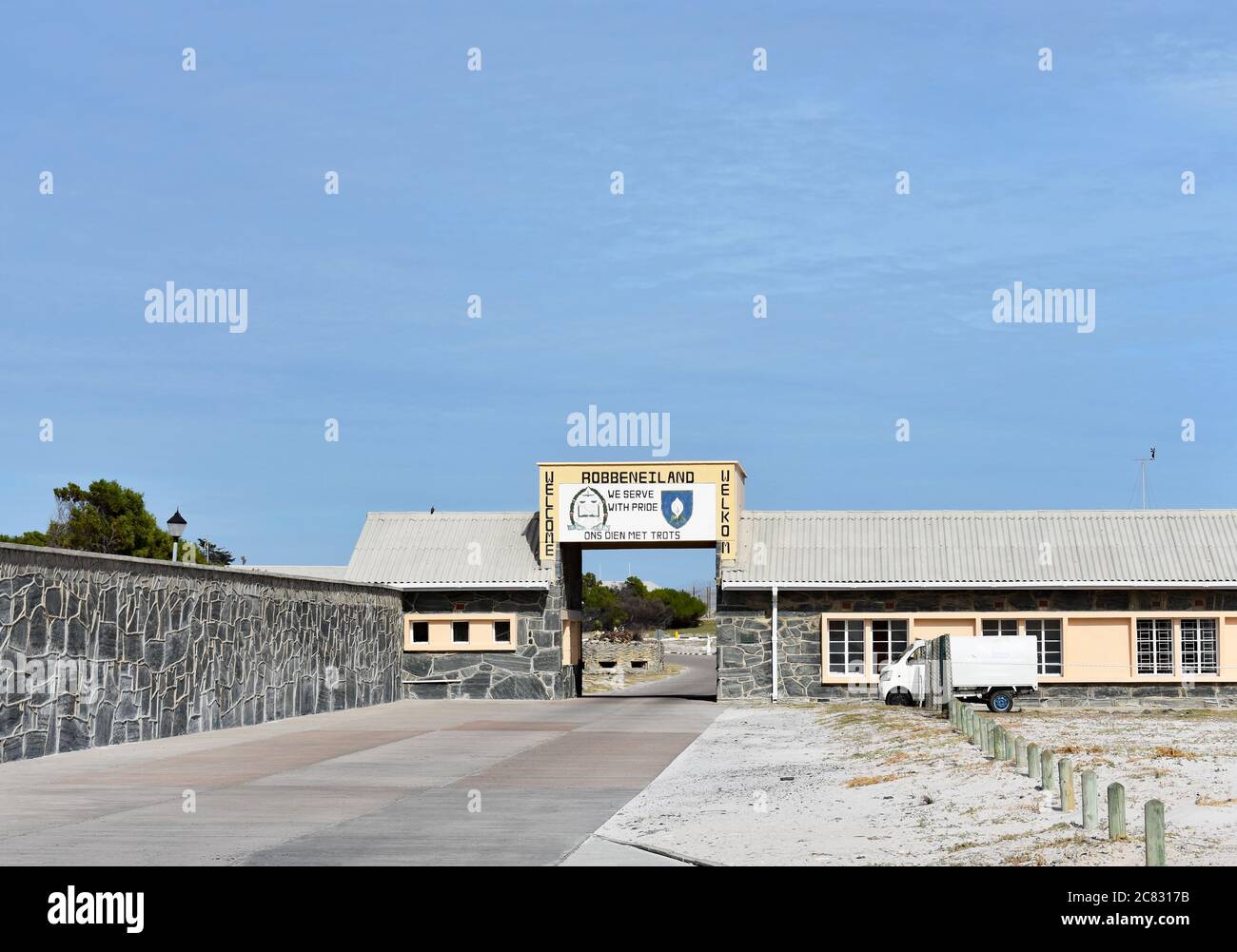 Le panneau d'entrée de Robben Island, un site classé au patrimoine mondial de l'UNESCO. Le panneau est au-dessus d'une route et à côté de divers bâtiments contre un ciel bleu. Banque D'Images