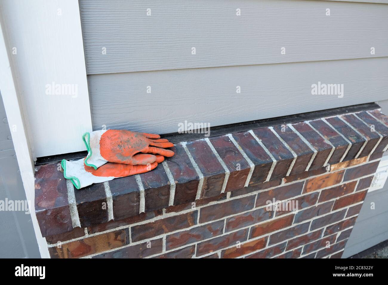 Paire de gants de travail orange pour jardin avec de la saleté sur une corniche de briques à l'extérieur; de la saleté incrustée sur les gants de cour utilisés pour le jardinage autour de la maison. Banque D'Images