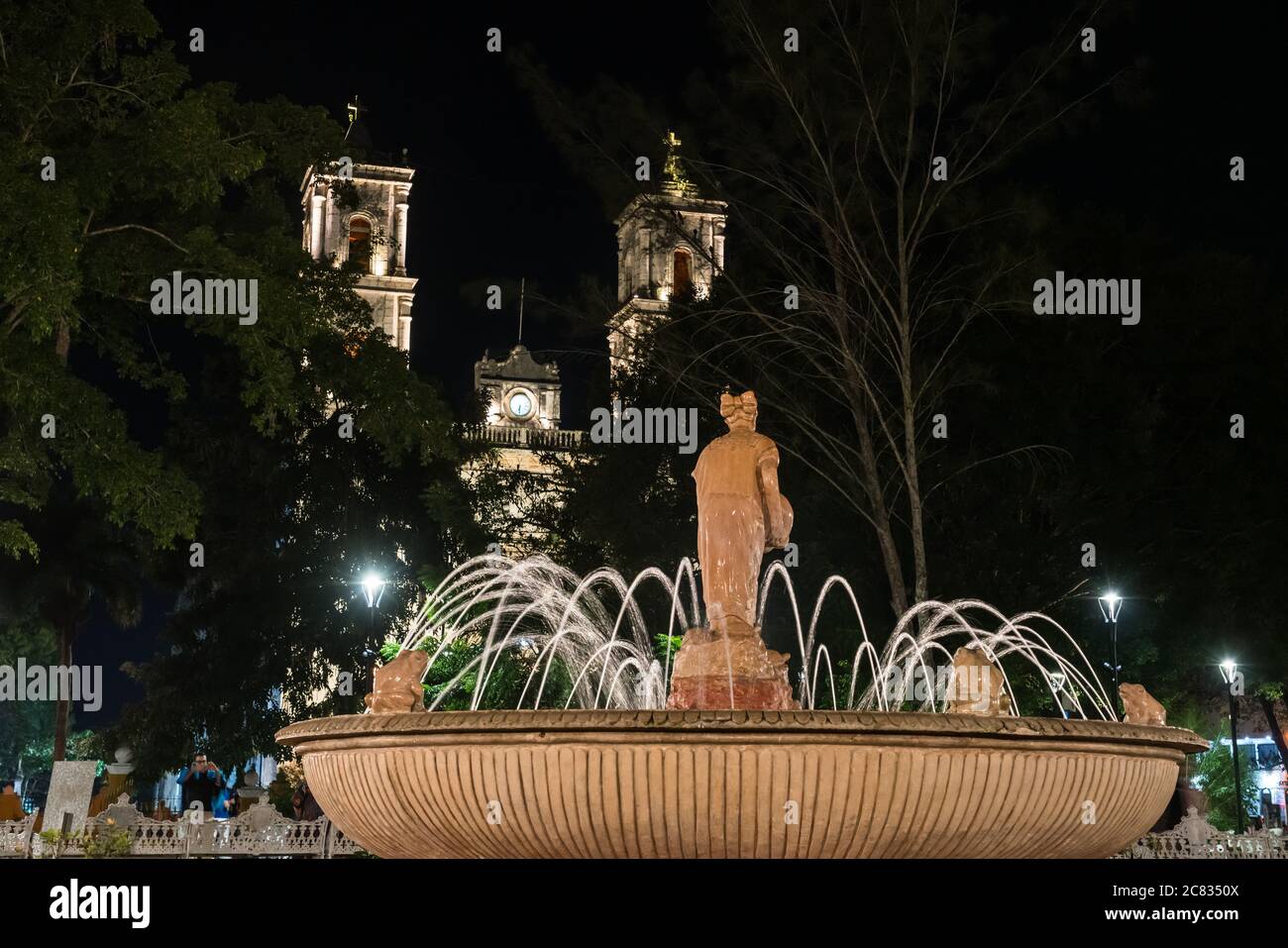 Une fontaine avec une statue d'une femme maya, éclairée la nuit, dans le parc Francisco Cantón Rosado. Derrière se trouve l'église de San Servasio. Valladolid, Yucatan, Banque D'Images
