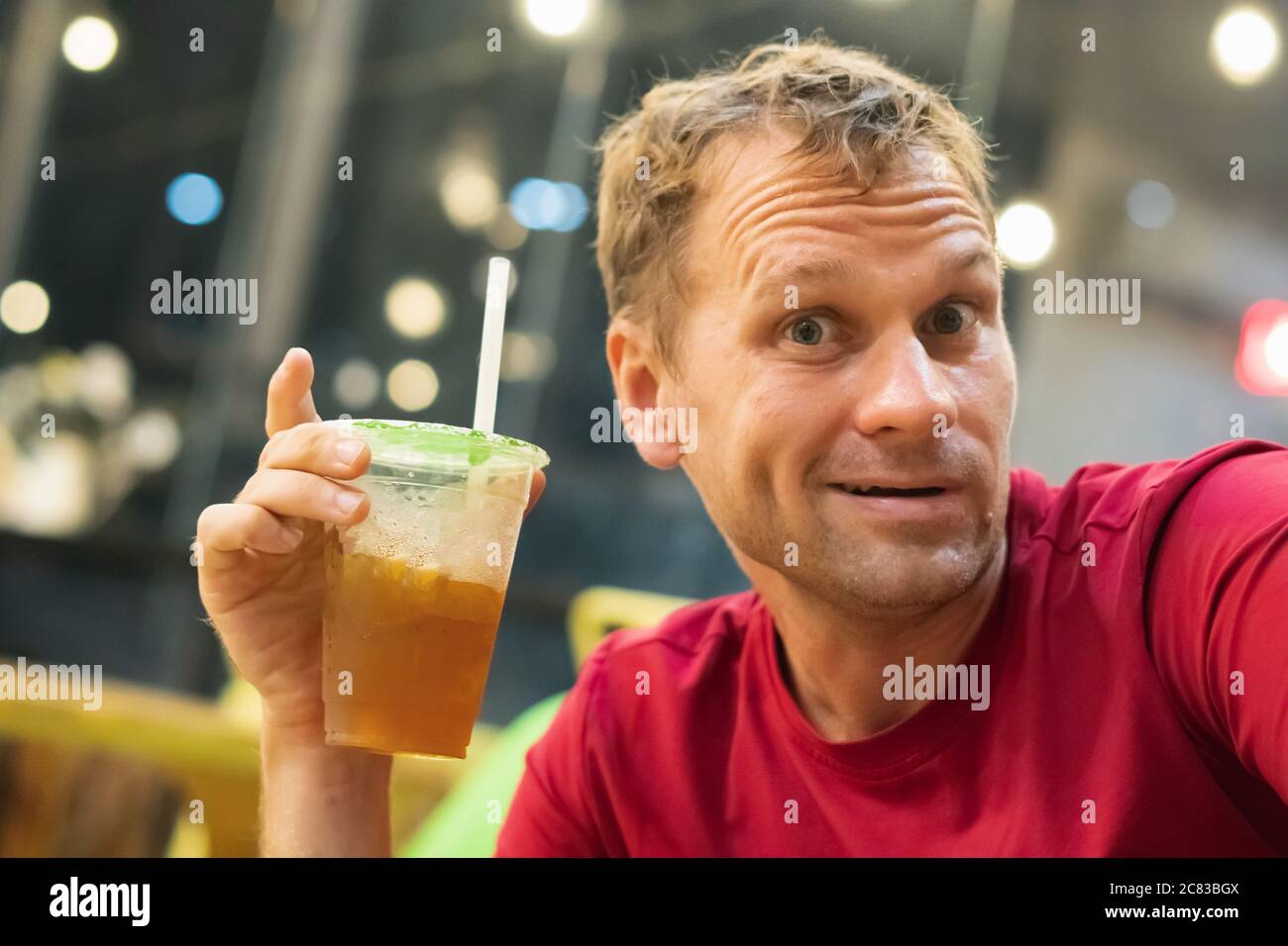 Vue de face d'un homme blond assoiffé qui boit de limonade, thé aux fruits, thé glacé kombucha avec pêche et citron, boissons d'orange bien-être dans une tasse en plastique Banque D'Images