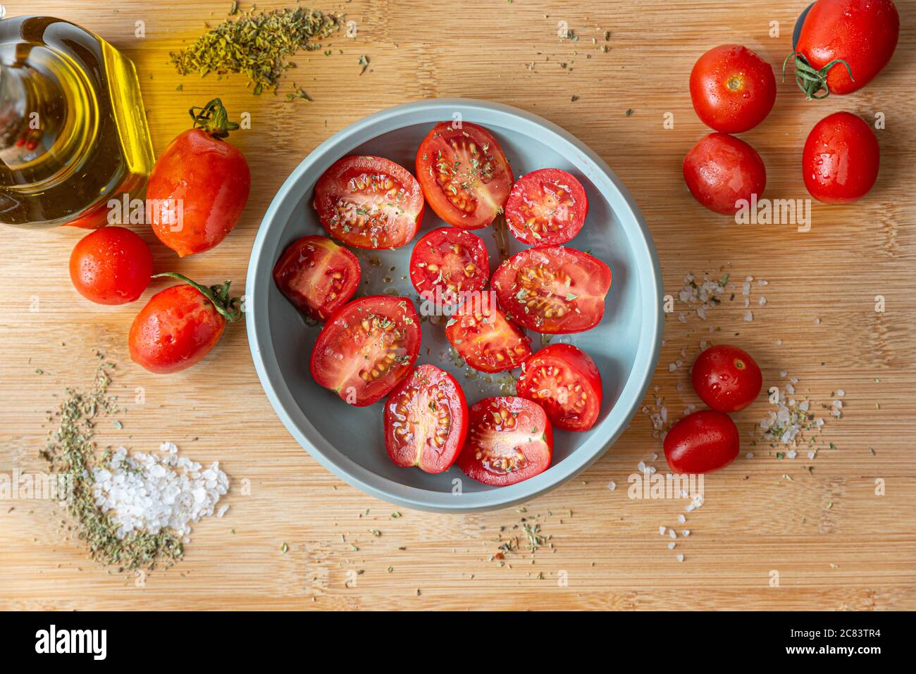 Naples, Italie. Image culinaire d'un bouquet de tomates dans un petit bol turquoise sur une planche à découper en bois avec du sel grossier, de l'origan et une cruelle à l'huile de verre Banque D'Images