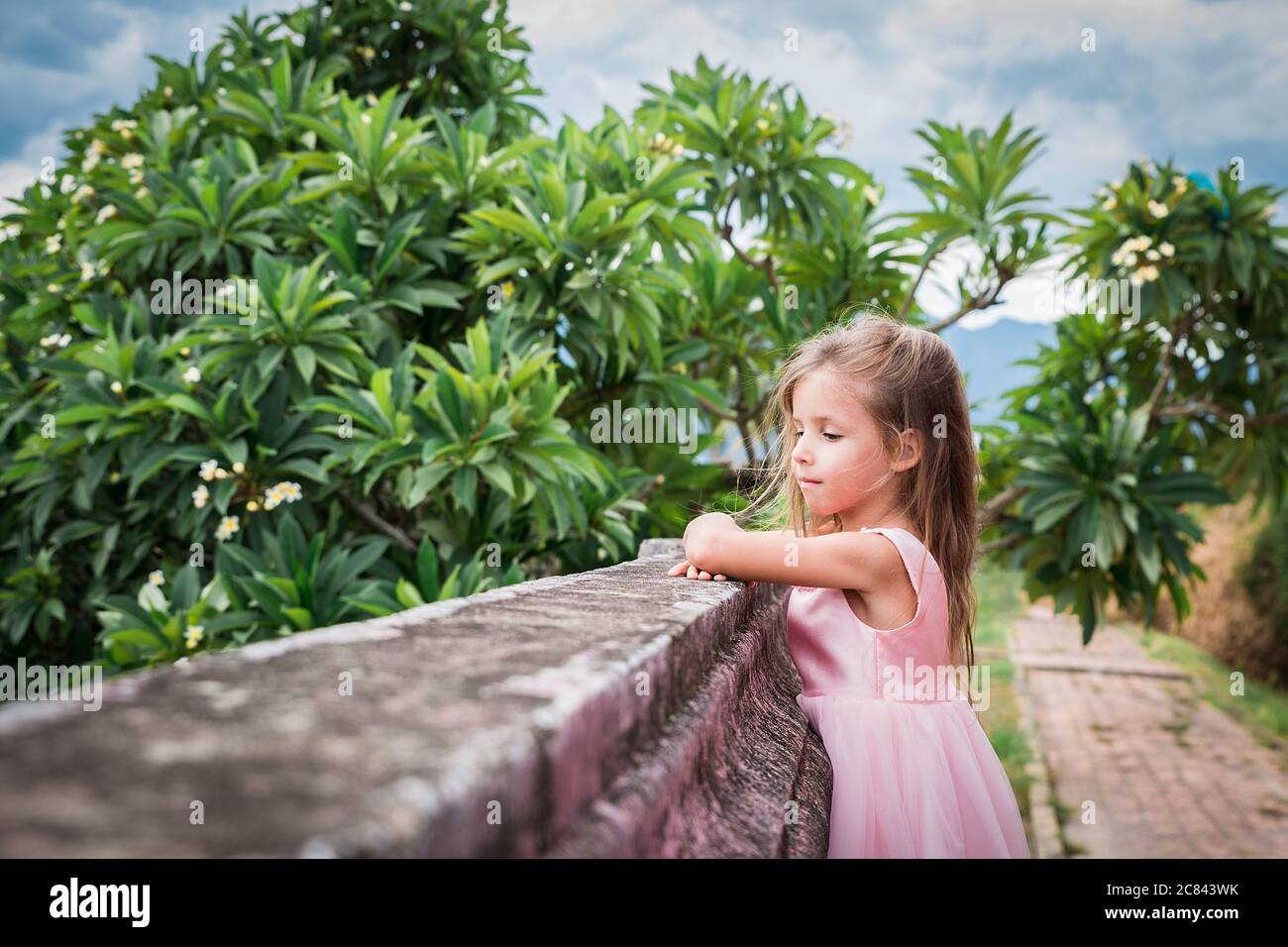 portrait d'une petite fille heureuse en robe rose à l'extérieur, près du mur Banque D'Images