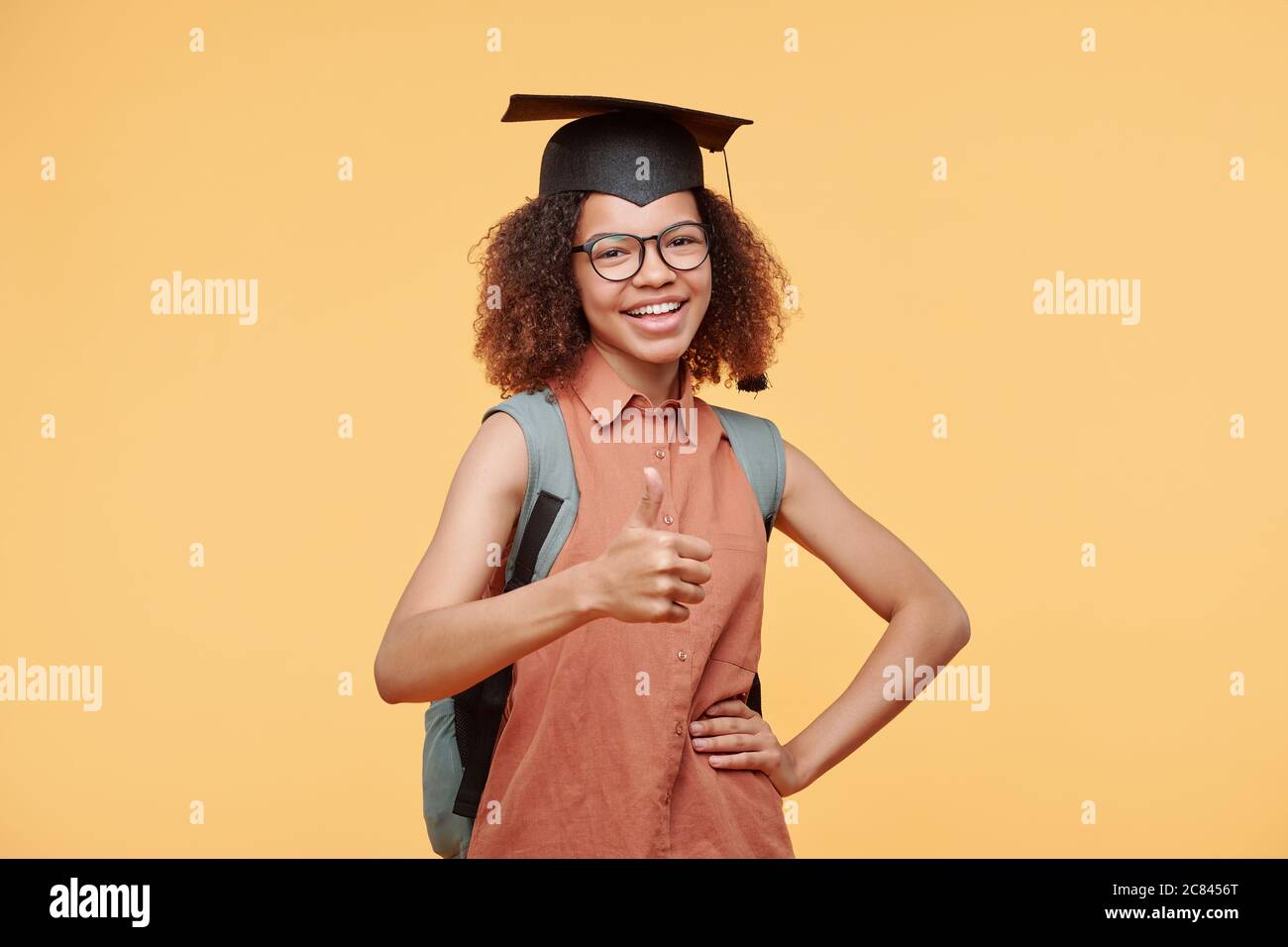 Portrait d'un étudiant noir joyeux et satisfait en casquette tenant la main  sur la hanche et montrant le pouce vers le haut sur fond jaune Photo Stock  - Alamy