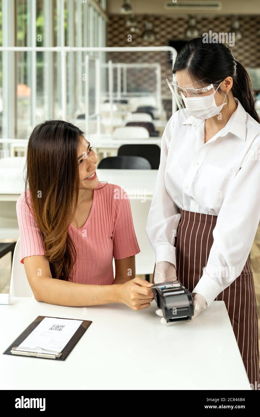 Une cliente asiatique fait le paiement par carte de crédit sans contact après avoir mangé dans un nouveau restaurant social distance normal pour réduire le contact. Contact en ligne Banque D'Images