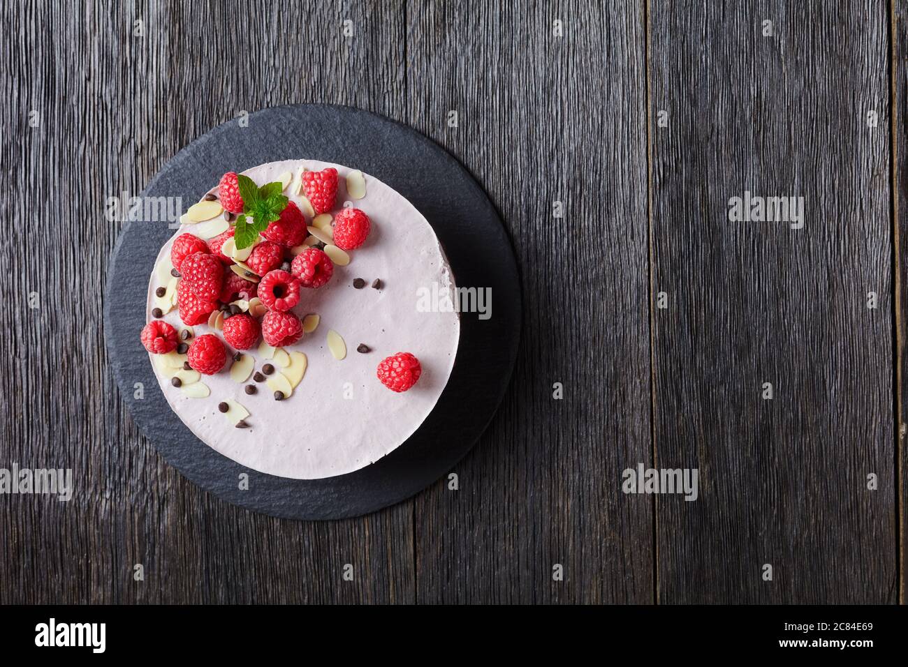 gâteau à la mousse framboise sur une assiette noire ardoise sur une table en bois sombre, vue sur le paysage depuis le dessus, plat, espace libre Banque D'Images