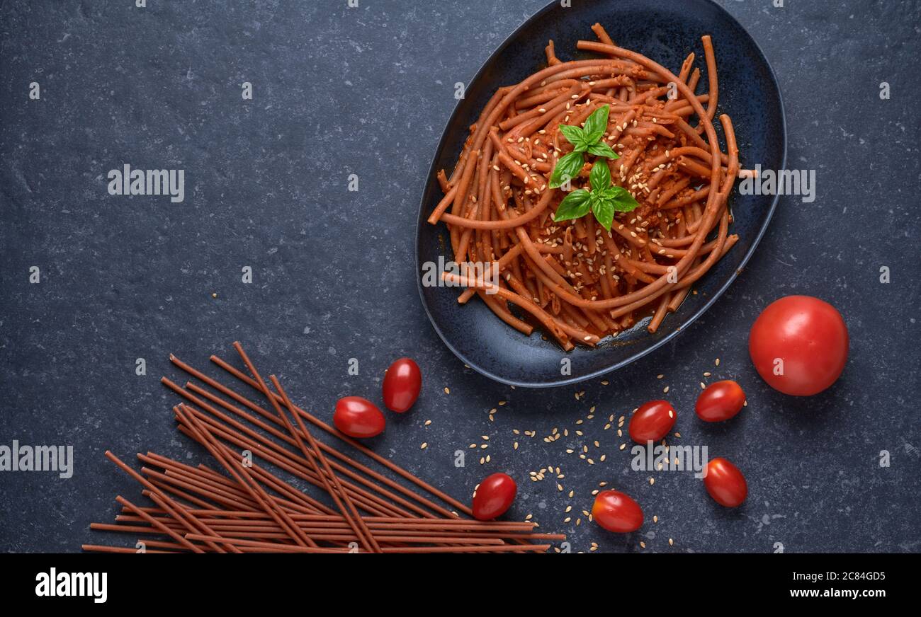 Bolognese vegan Bucatini, sans viande, avec sauce soja, tomates, graines de sésame et basilic frais, dans une assiette en pierre noire sur fond sombre. Banque D'Images