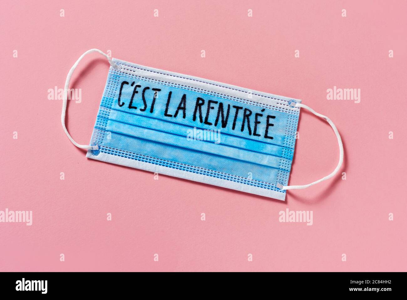 vue à grand angle d'un masque chirurgical bleu avec le texte de retour à l'école écrit en français, sur fond rose, décrivant la nécessité de prévenir l'infection Banque D'Images