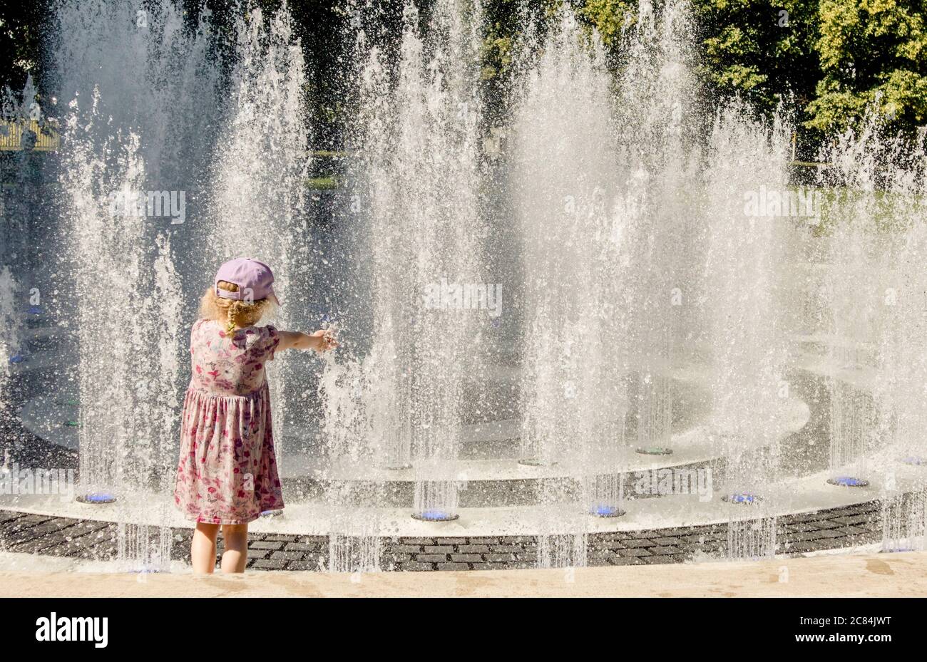 Les enfants jouent dans la fontaine d'eau dans le parc public, s'amusent par une chaude journée d'été ensoleillée. Banque D'Images