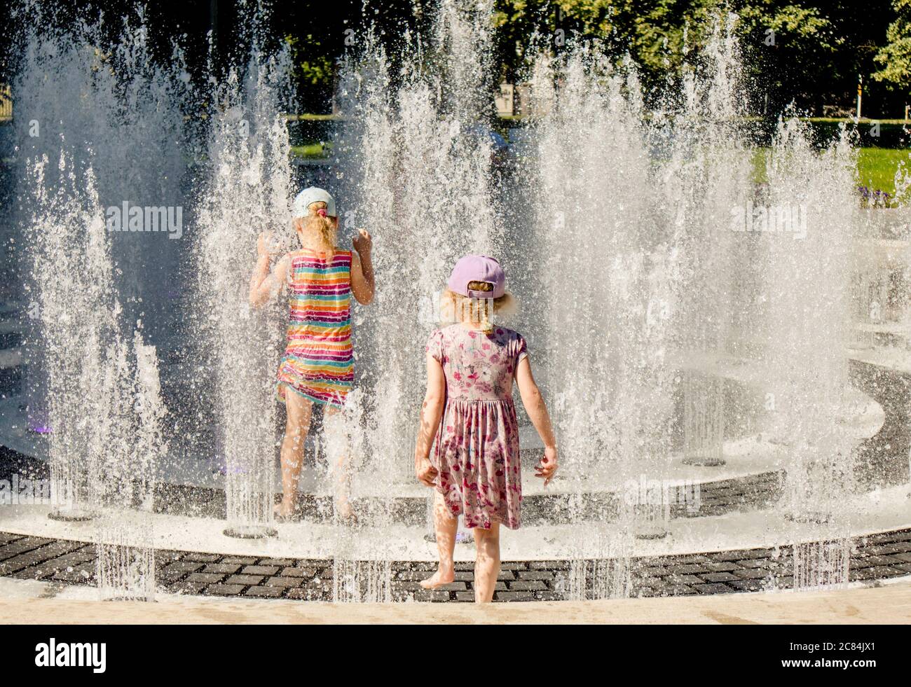 Les enfants jouent dans la fontaine d'eau dans le parc public, s'amusent par une chaude journée d'été ensoleillée. Banque D'Images
