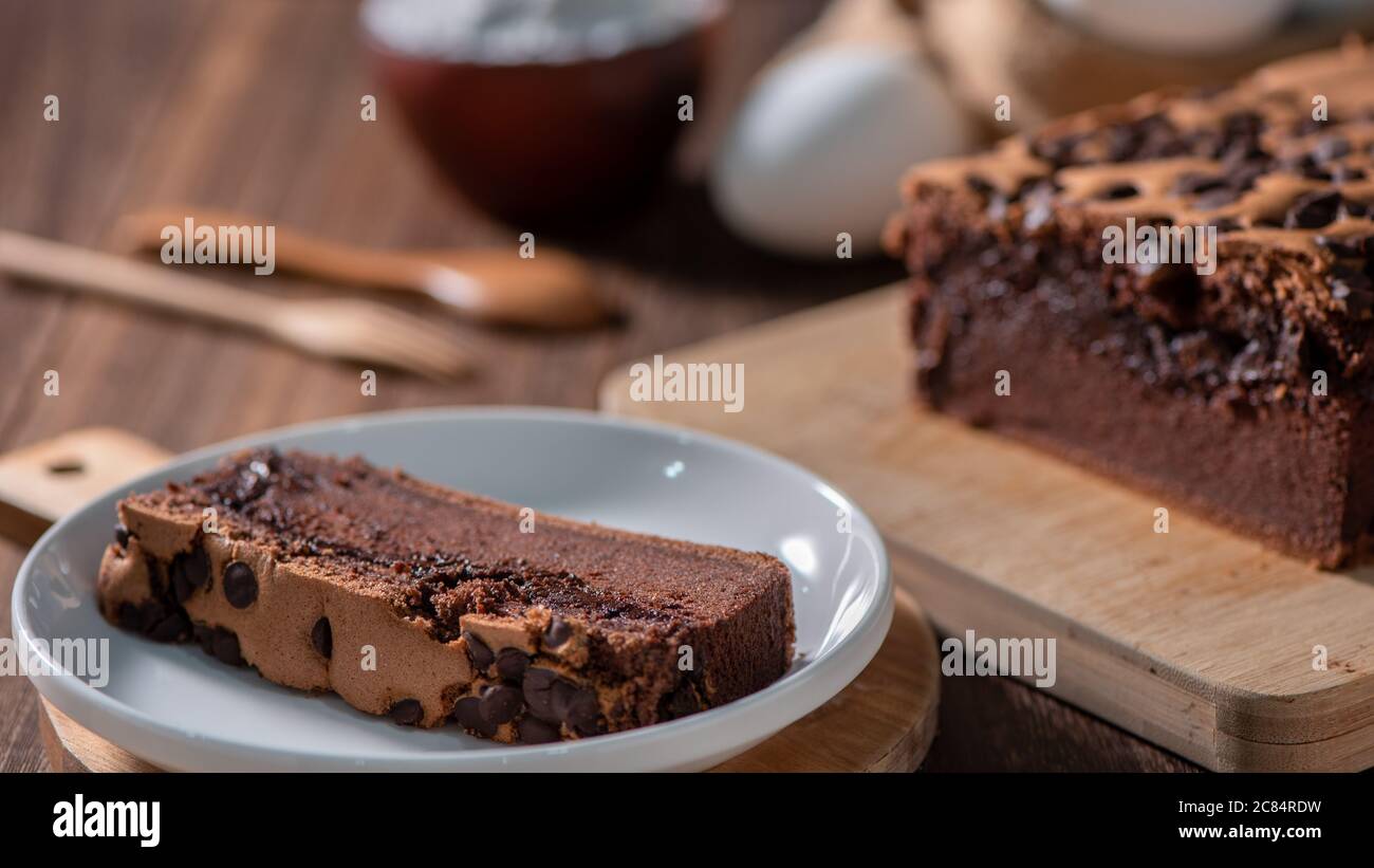 Gâteau éponge traditionnel taïwanais au goût de chocolat (taïwanais castella kasutera) sur une table de fond en plateau de bois avec les ingrédients, gros plan. Banque D'Images