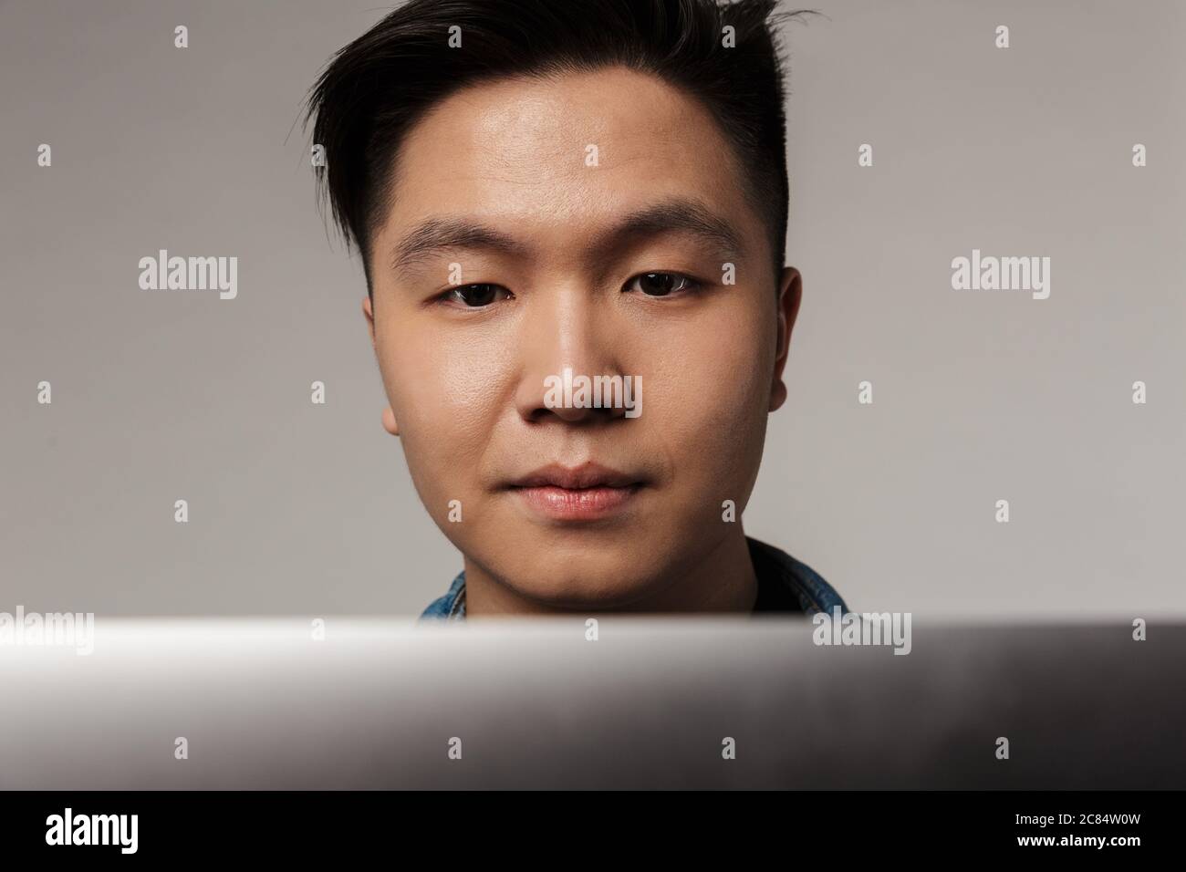 Gros plan sur un beau homme asiatique concentré travaillant avec un ordinateur portable isolé sur fond gris Banque D'Images