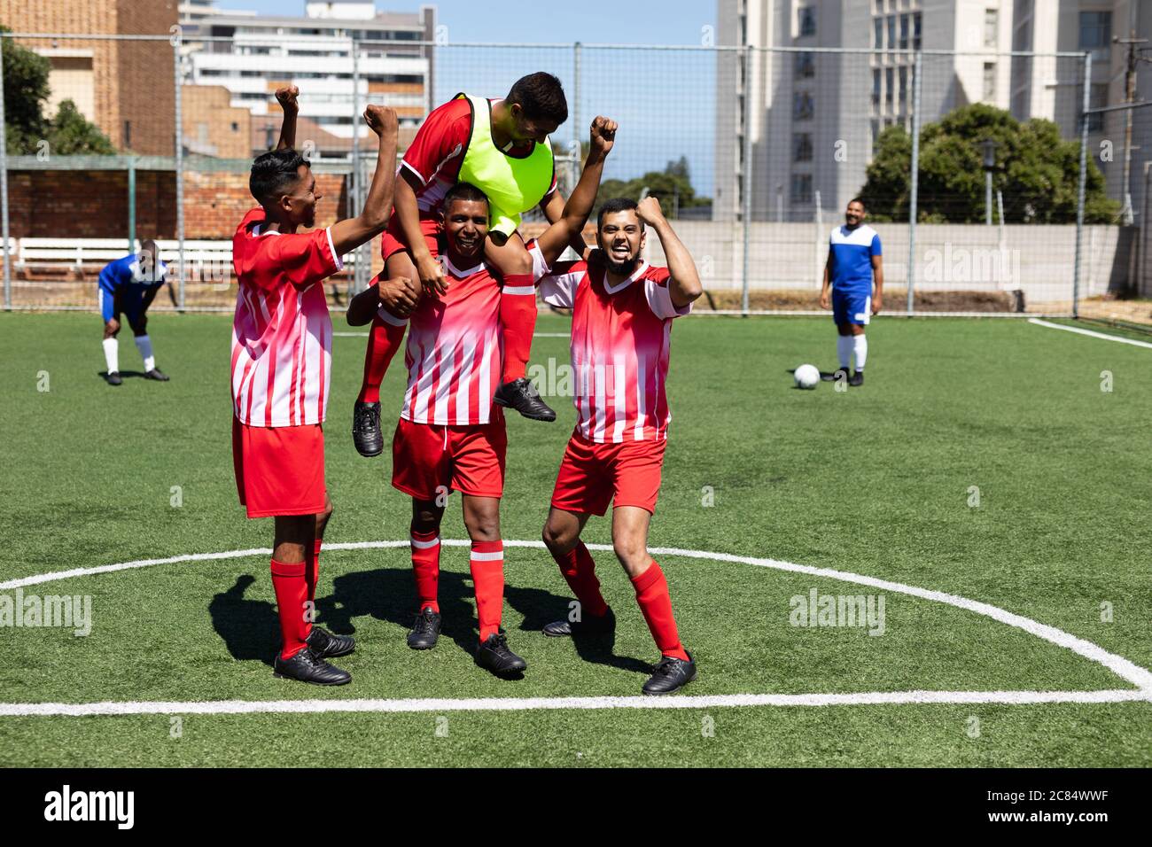 Deux équipes multiethniques de joueurs de football masculin de cinq a côté portant une bande d'équipe jouant un match sur un terrain de sport au soleil, célébrant Victory carr Banque D'Images