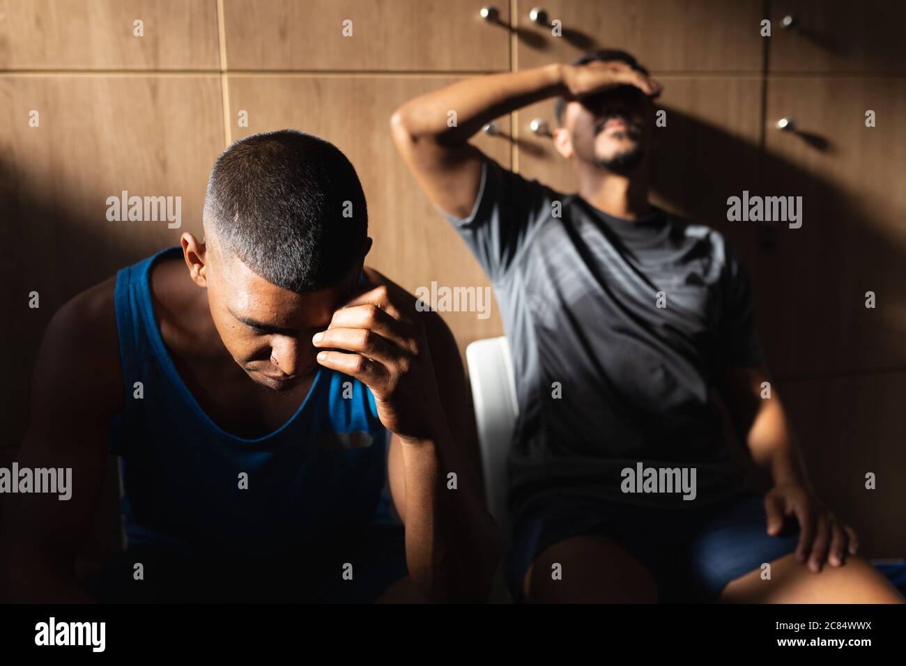 Deux joueurs de football de race mixte, hommes, portant des vêtements de sport assis dans le vestiaire pendant une pause dans le match, se reposant tenant leur tête étant disappo Banque D'Images