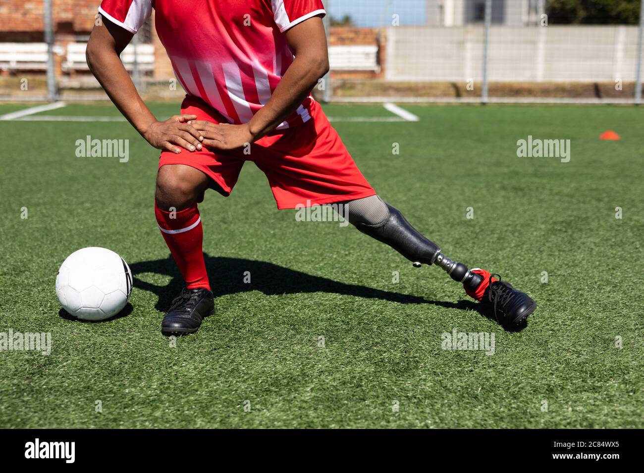 Coupe basse d'un joueur de football masculin de course mixte avec jambe prothétique portant un entraînement d'équipe sur un terrain de sport au soleil, en s'échauffant s'étirant l Banque D'Images