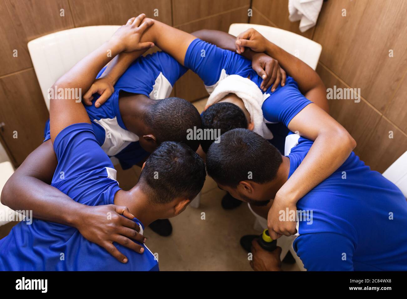 Groupe multiethnique de joueurs de football masculins portant une bande d'équipe dans le vestiaire pendant une pause dans le jeu, debout dans le caucus se motivant mutuellement. Banque D'Images