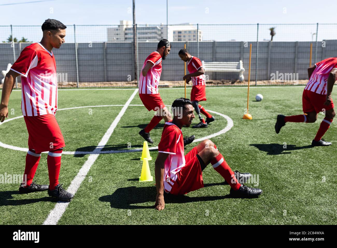 Équipe multi-ethnique de cinq joueurs de football de côté, portant un entraînement de bande d'équipe sur un terrain de sport au soleil, en cours d'échauffement d'un joueur avec Banque D'Images