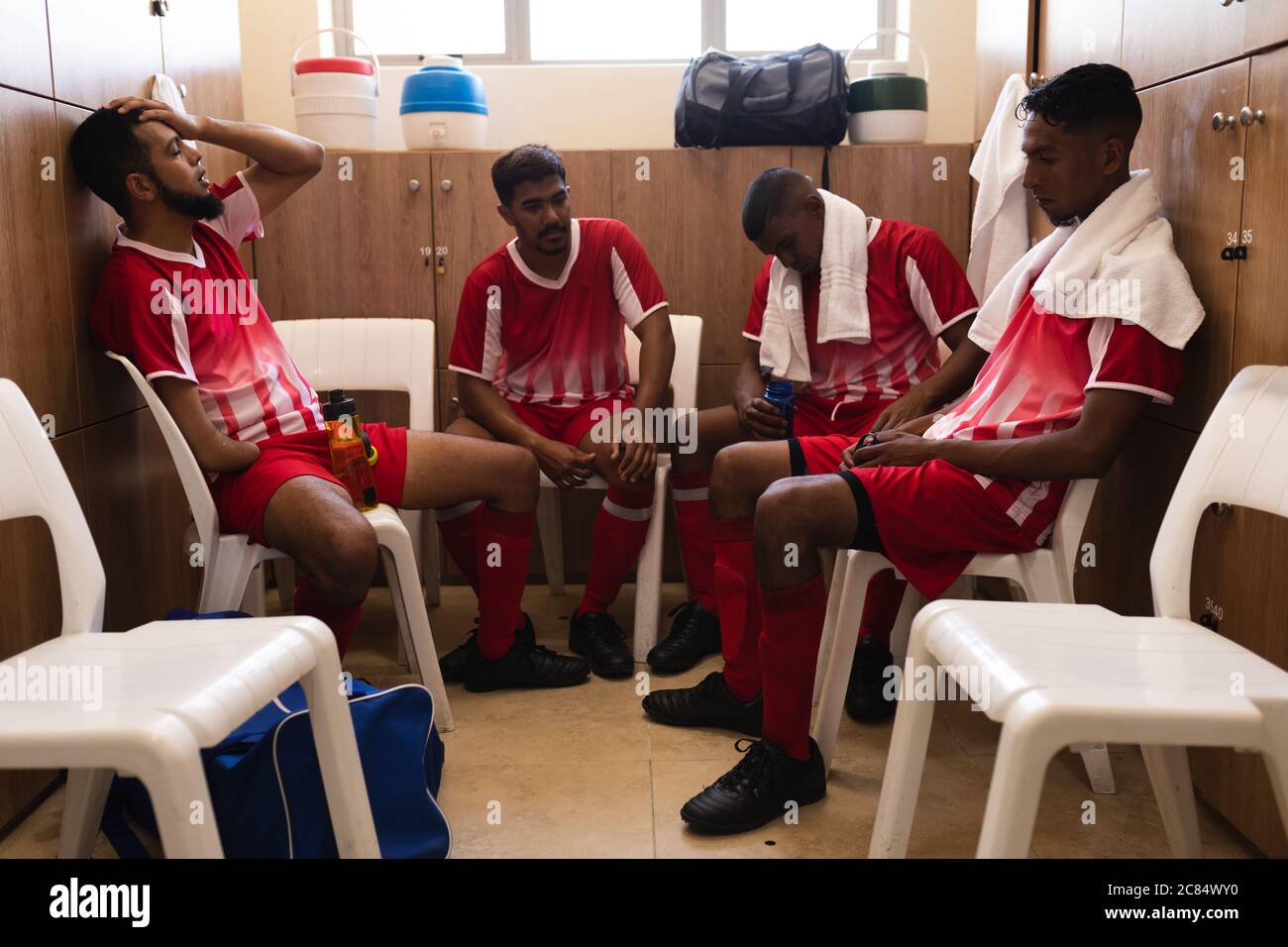 Groupe multiethnique de joueurs de football masculins portant une bande d'équipe assis dans le vestiaire pendant une pause dans le jeu, déçus par la serviette autour de leur Banque D'Images
