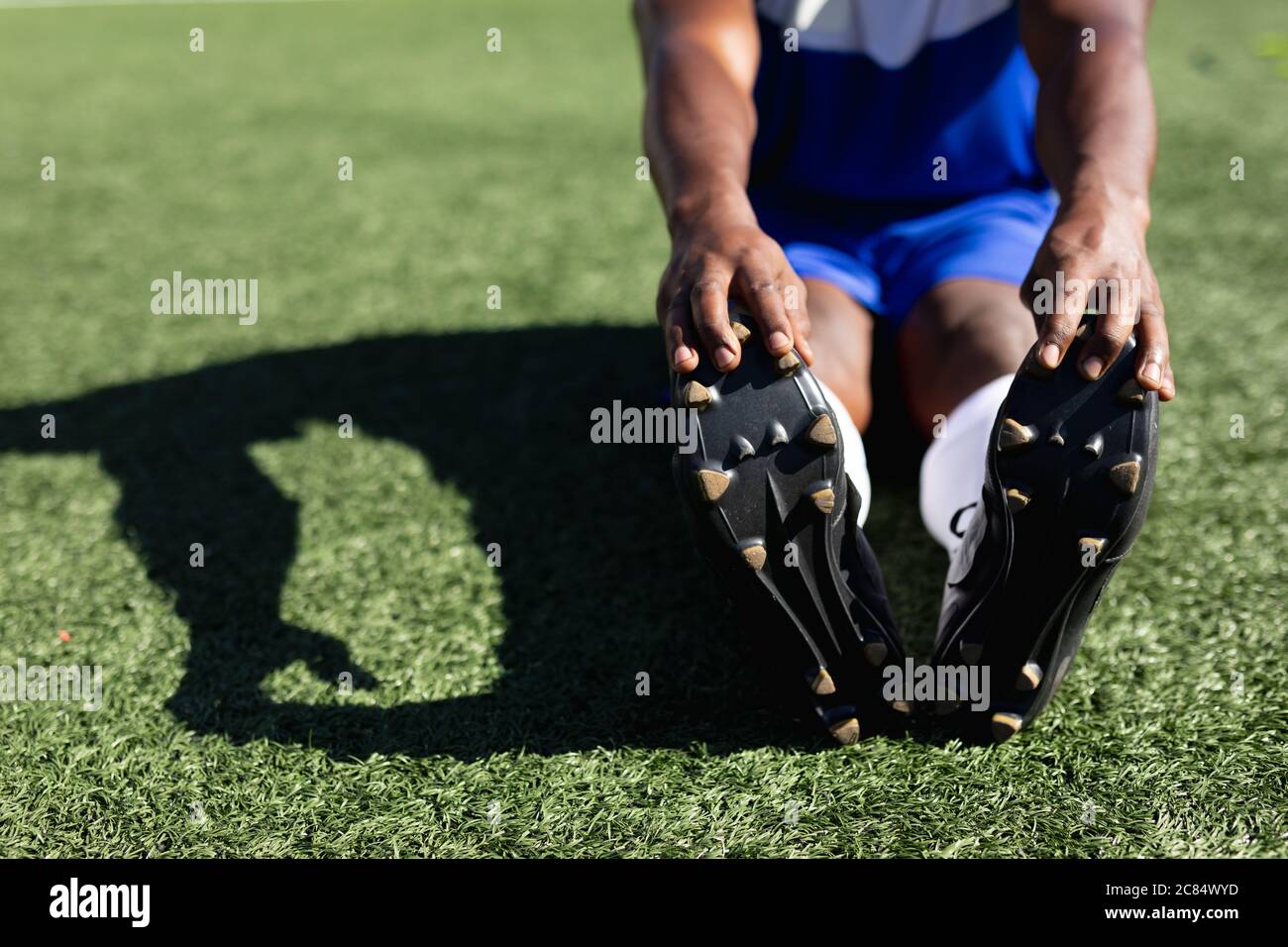 Joueur de football masculin de course mixte portant un entraînement d'équipe sur un terrain de sport au soleil, en s'échauffant s'étirant les jambes. Banque D'Images