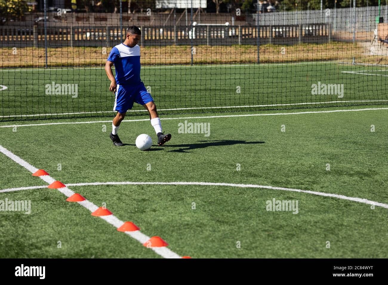 Course mixte masculin cinq un joueur de football latéral portant un entraînement de bande d'équipe sur un terrain de sport au soleil, s'échauffe avec le ballon. Banque D'Images