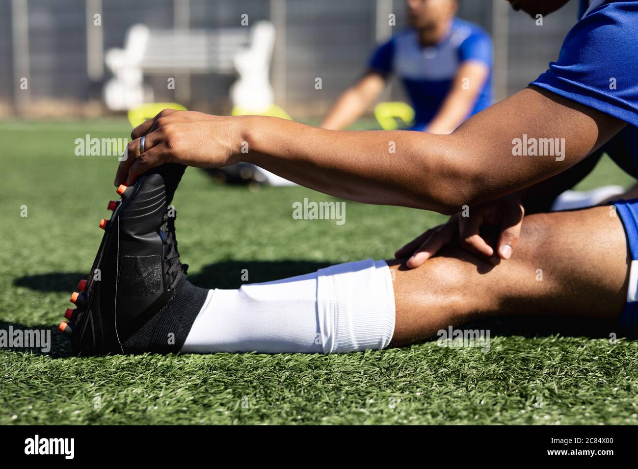 Joueur de football masculin de course mixte portant un entraînement d'équipe sur un terrain de sport au soleil, en s'échauffant s'étirant les jambes. Banque D'Images
