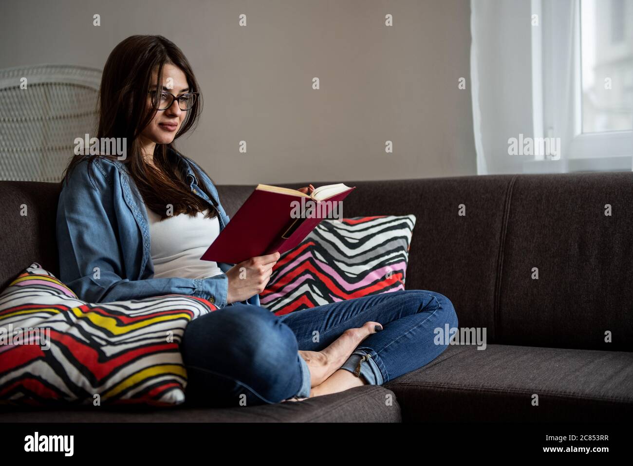 Une femme heureuse et détendue lisant un livre assise sur un canapé à la maison. Une femme heureuse et détendue lisant un livre assise sur un canapé à la maison. Banque D'Images
