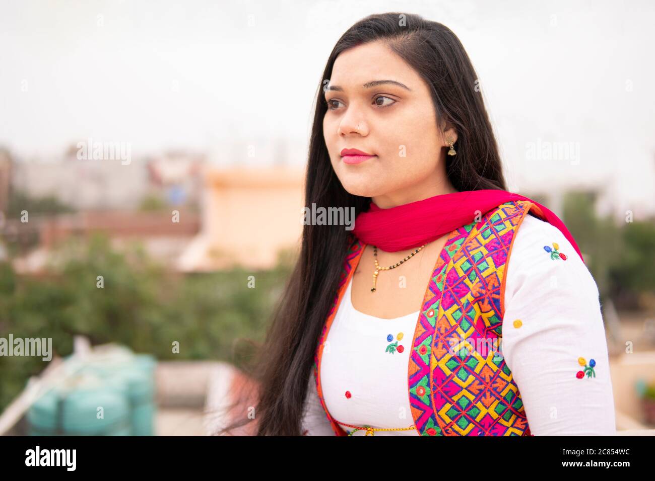 Portrait de la jeune femme indienne belle regardant loin et pensant avec le sourire. Elle se tient près de la rambarde sur le toit à l'heure de la journée. Banque D'Images