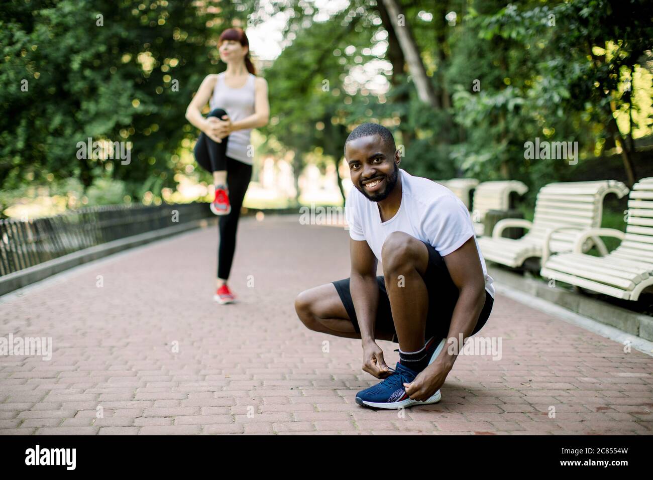 Beau sourire africain homme laçage ses chaussures et se préparant à courir  et de sport à l'extérieur dans le parc de la ville avec sa petite amie,  jolie femme caucasienne Photo Stock -