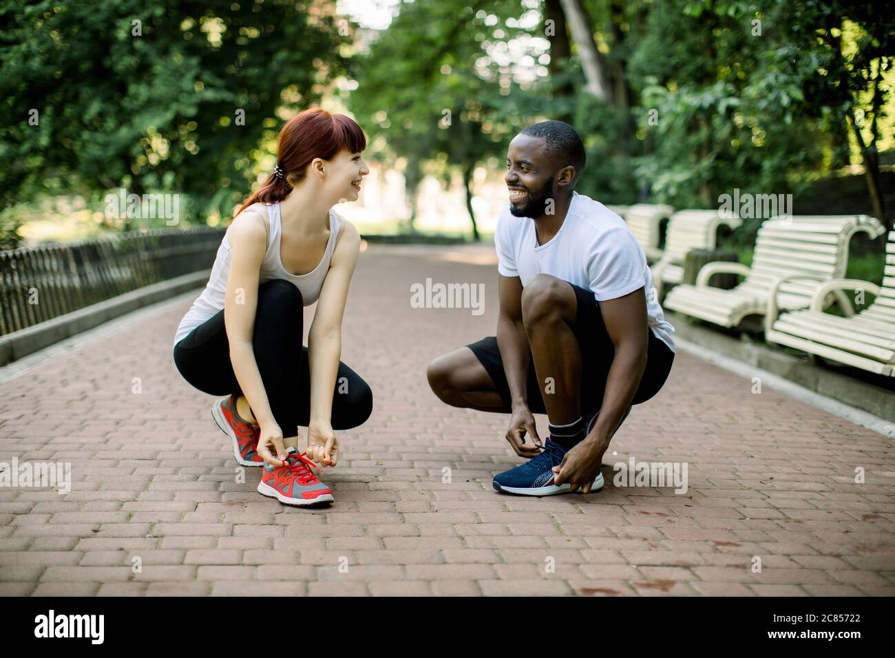 Jeune couple actif multiethnique souriant, homme beau africain et jolie  femme caucasienne, nouant les lacets de chaussures d'entraîneur avant de  courir dans le parc, regardant Photo Stock - Alamy