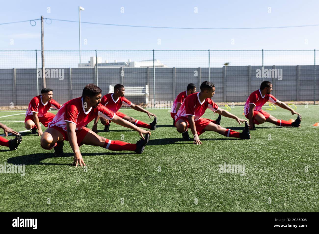 Équipe multiethnique de cinq joueurs de football de côté, portant un entraînement de strip d'équipe sur un terrain de sport au soleil, s'échauffer. Banque D'Images