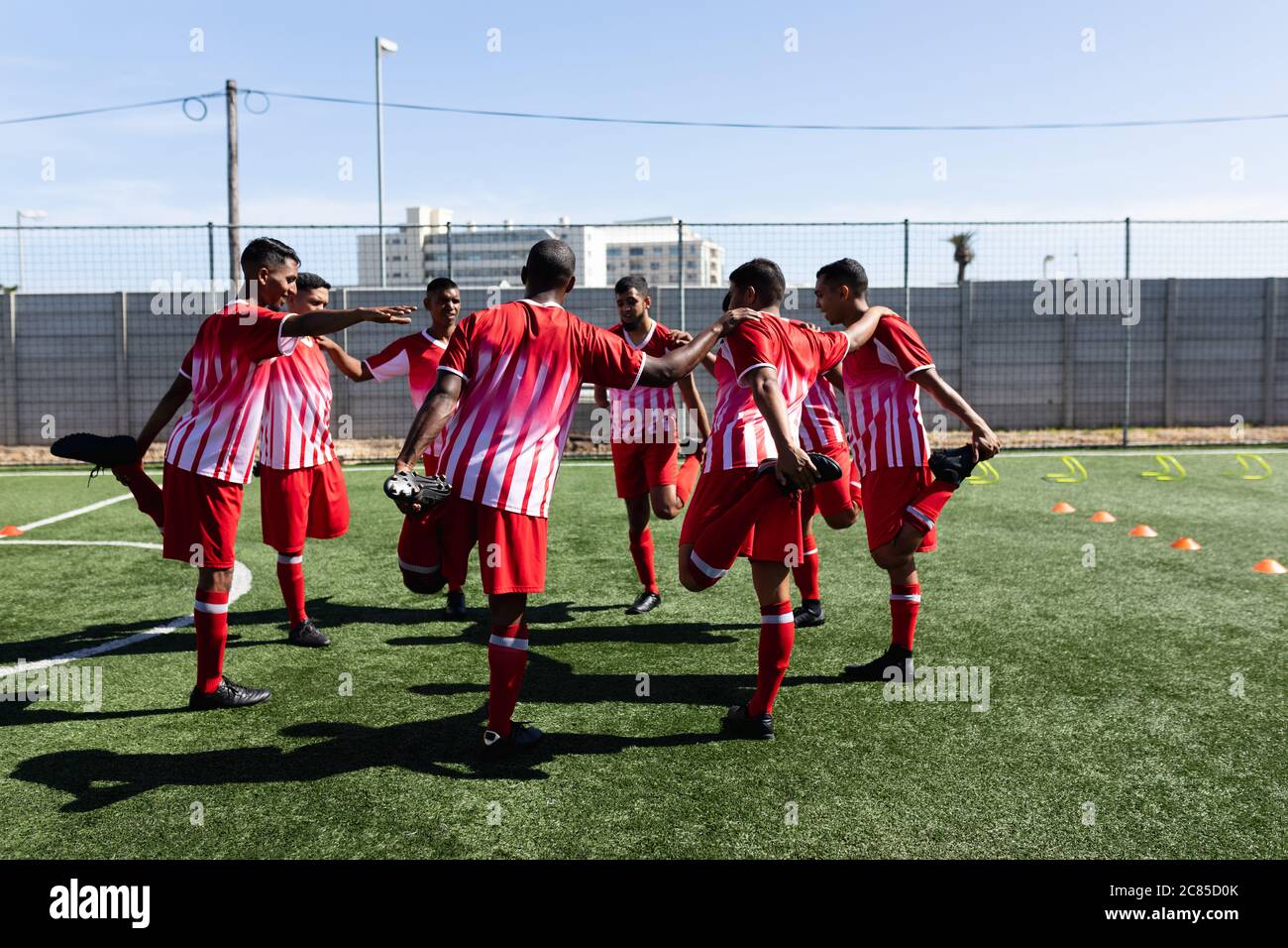 Équipe multiethnique de cinq joueurs de football de côté, portant un entraînement de bande d'équipe sur un terrain de sport au soleil, se réchauffant debout en bouclette Banque D'Images