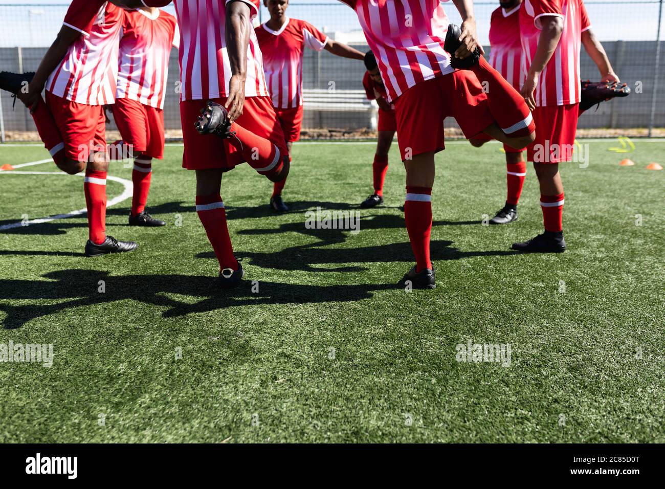 Équipe multiethnique composée de cinq joueurs de football de côté, portant un entraînement sur piste d'équipe sur un terrain de sport au soleil, se réchauffant debout en cercle Banque D'Images