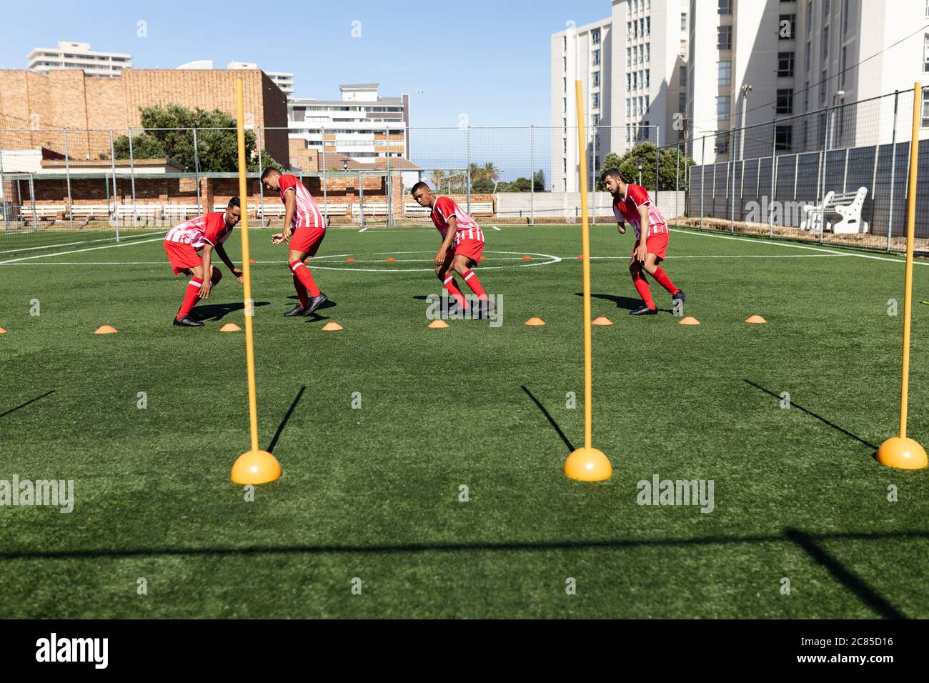 Équipe multiethnique de joueurs de football de cinq a côté, portant un entraînement de strip d'équipe sur un terrain de sport au soleil, en cours d'échauffement. Banque D'Images