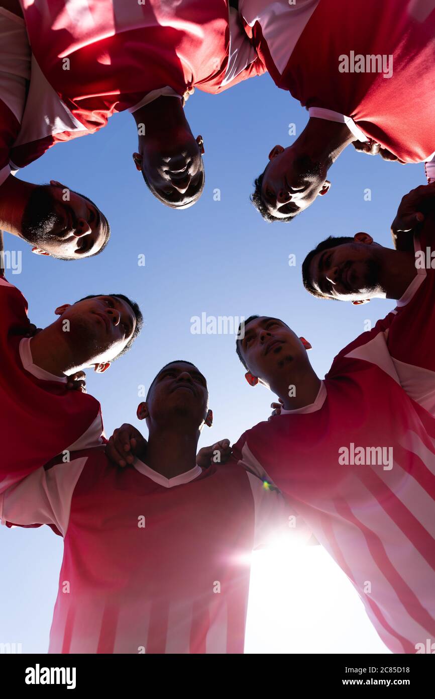Vue en contre-plongée d'une équipe multi-ethnique composée de cinq joueurs de football de côté portant un entraînement de bande d'équipe sur un terrain de sport au soleil, debout dans un huddl Banque D'Images